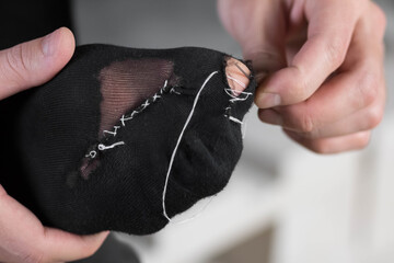 A man sews a black torn sock with white threads. Closeup. Isolated on a white background