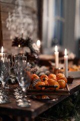 a wooden table with wine glasses and tangerines, bottles of wine, burning candles. Festive Christmas atmosphere