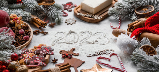 Happy New Year 2023. Banner with kitchen utensils, Christmas decorations, cinnamon, gingerbread and spruce on a marble background. A greeting card for Christmas. The concept of cafes and restaurants.