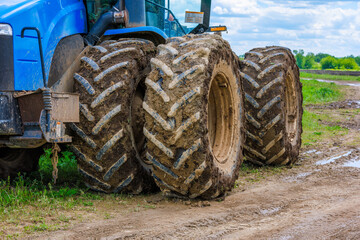 double wheels of agriculture tractor clogged with earth at summer day, close-up