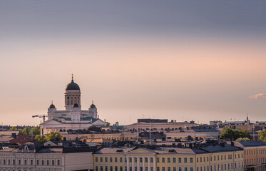 Fototapeta na wymiar Helsinki, Finland - July 19, 2022: Sunset over city landscape with cathedral in half lighted sky. Lookiing north fron the sea