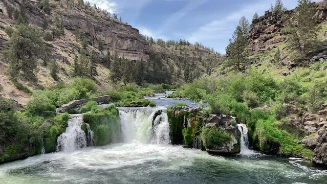 The Stunning cascade of Steelhead Falls as the Deschutes River flows through a steep red rock canyon. The landscape is lush green - Nr Terrebonne, Oregon, USA