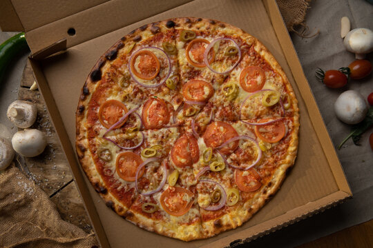 Traditional italian food. Delicious fresh pizza with cheese, tomatoes and onion on wooden background with ingredients, flat lay.