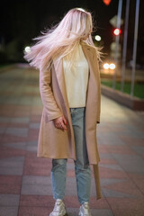 Obraz premium Portrait of a young beautiful fair-haired girl in a beige coat close-up in the night city. There is artistic noise.