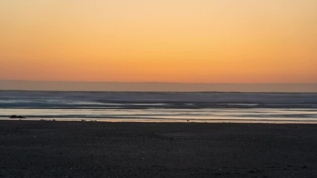 Bright yellow sun sets over the horzion from orange sky - timelapse