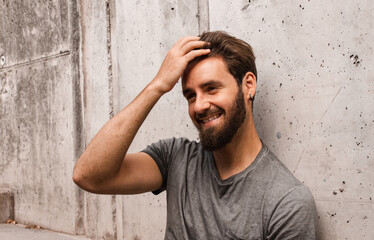 Portrait of a bearded man touching his hair and laughing in a wall. Urban city photography. Handsome and attractive caucasian hipster man.