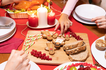 Overhead view of party dinner table at Christmas time with hands reaching for holiday treats,...