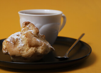 Homemade custard eclairs with a cup of tea on an orange table. View from above