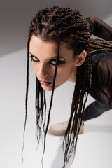 high angle view of woman with pigtails and futuristic makeup looking at camera on grey background.