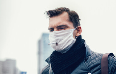serious man in a protective mask smokes standing on the street.