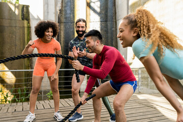 Multiracial group of people exercising with battle rope and cheering each other on. Fitness concept
