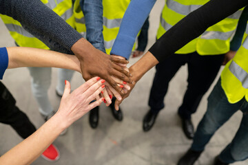 Close up multiracial group of workers wearing reflective vests with their hands together showing unity. Teamwork concept