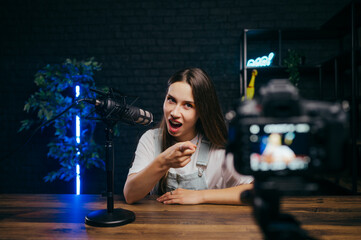 Expressive female blogger recording videos in studio, speaking into professional microphone and...