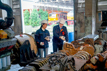 Wide shot of Caucasian and Asian factory worker discuss together in front of stack and layer of metal part of machine that use for industrial or other work relate to the train.