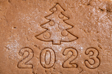 Fototapeta na wymiar The figures of the year 2023 and the Christmas tree are cut out of gingerbread dough. We cook homemade gingerbread at home. New Year's card from the test.