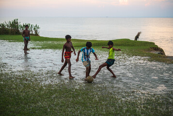 South asian rural teenage boys playing football at a wet ground near a river just before the fifa...