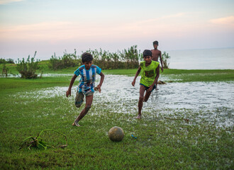 South asian rural teenage boys playing football at a wet ground near a river just before the fifa...