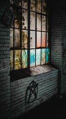 Vertical shot of an multicolor window in an abandoned building with a pentagram graffiti under it