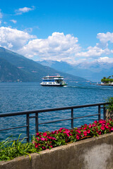 White boat ferry cruising around the shore of Bellagio, the Pearl of Lake Como, one of the most famous and picturesque towns in Lombardy, Italy, that boasts unparalleled shoreline and Alpine views.