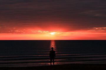 The shore of the Caspian Sea at sunset, pink-orange clouds, water, beach, summer, a person stands on the shore. Silhouette of a man.