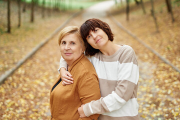 Caucasian mother and her daughter staying in adorable autumn park. Portrait of senior pensioner mom and adult cheerful daughter spending time together outdoor in falling season. High quality photo