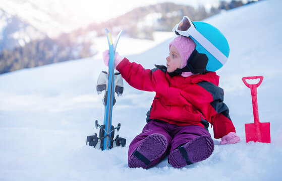 Little Girl Sit On Snow, Hold Mountain Ski In Sport Outfit