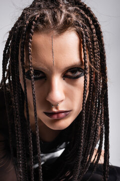 portrait of young woman with futuristic makeup and dreadlocks looking at camera isolated on grey.
