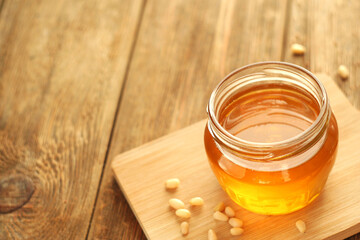 A transparent jar of honey stands on a board on a wooden table. Nearby are pine nuts. Copy space. selective focus