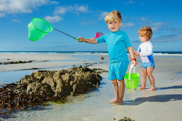 Two kids with butterfly net on the sand beach catching crabs