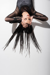 top view of futuristic woman with braids touching head while lying on white background with shadow.