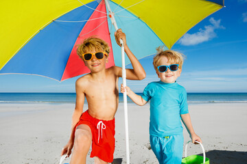 Two boys in sunglasses under parasol on a sand ocean beach
