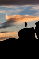 An orange-pink sunset on the black sea against the background of various black mountains, a small silhouette of a person stands on the mountain. Landscape. Vertical orientation.