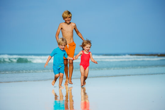 Group of three children run on sand beach holding hands