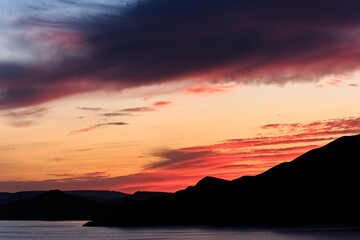 Orange sunset on the black sea against the backdrop of mountains and rocks.