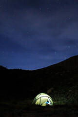 Mountains, night, luminous tent on the background of mountains. Vertical orientation.