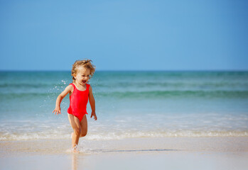 Fototapeta premium Little cute girl run on the sand beach in ocean waves smiling