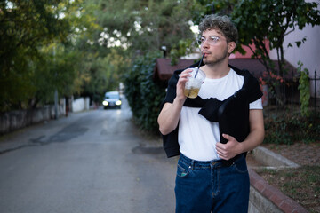 young man walking on modern street drinking cold drink, natural lighting photo of a person