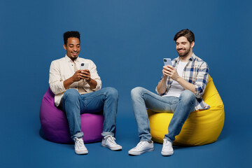 Full body young two friend happy men 20s wear white casual shirts together sit in bag chair hold in...