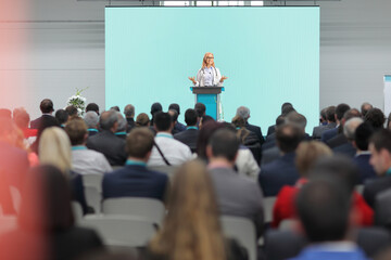 Female doctor giving a speech on a pedestal in front of an audience at a congress - obrazy, fototapety, plakaty