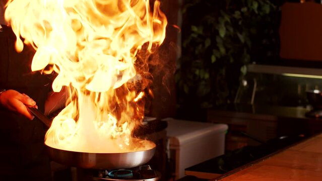 Cook preparing food in frying pan with fire