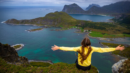 a girl with her hands raised celebrates at the top of a mountain enjoying the view of the lofoten...