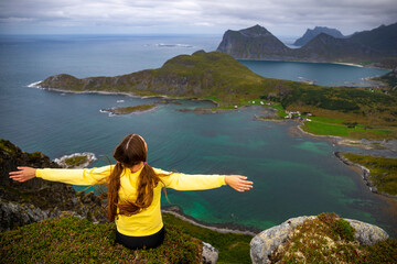 a girl with her hands raised celebrates at the top of a mountain enjoying the view of the lofoten...