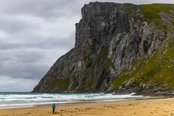 a girl walks alone on the famous kvalvika beach on the lofoten islands in norway; the famous beach surrounded by massive rugged mountains