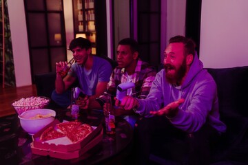 Three male friends playing video games and drinking beer in dark living room