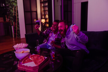 Two excited male friends gesturing as winners while playing video game in dark living room