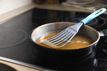 Frying pan with spatula and used cooking oil on stove