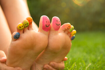 Naklejka premium Teenage girl with smiling faces drawn on toes outdoors, closeup