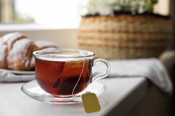 Tea bag in glass cup on white windowsill, closeup. Space for text