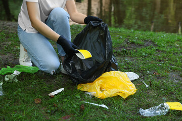 Woman with plastic bag collecting garbage in park, closeup