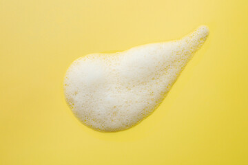 Drop of fluffy soap foam on yellow background, top view